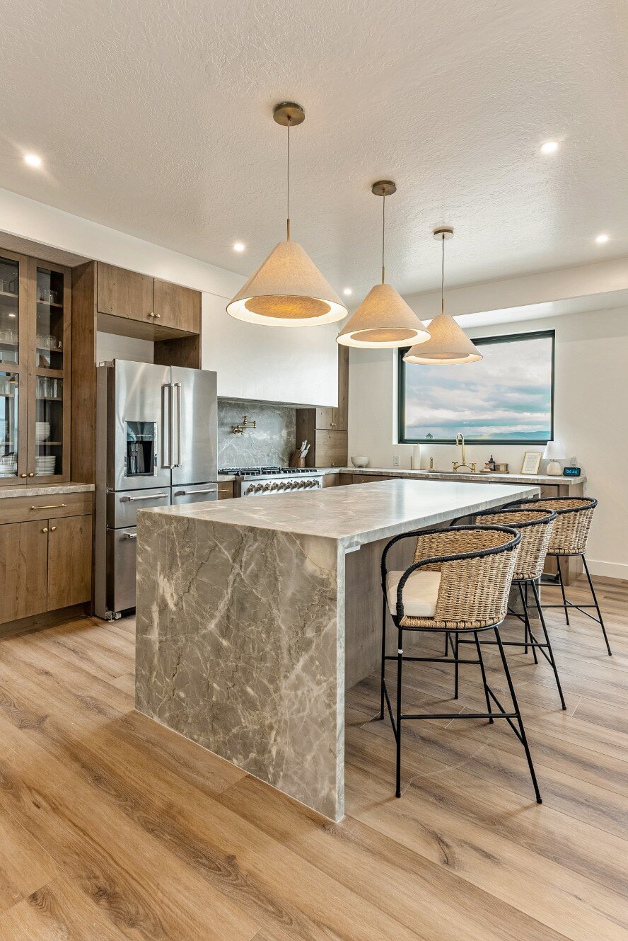 Kitchen Island with Barstools and View Out of Over-The-Sink Window in Bear Lake Custom Home by 10X Builders (Portrait)